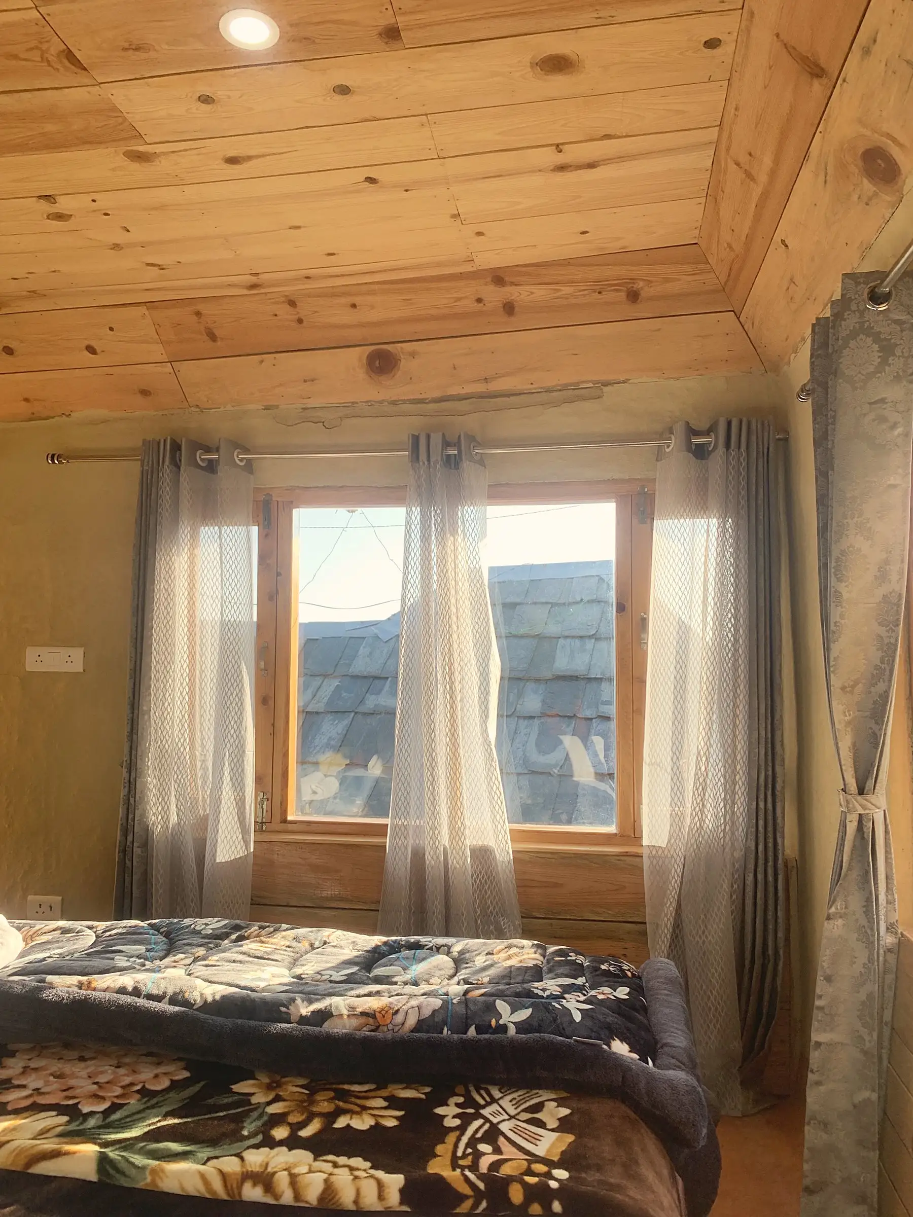 A bedroom lined in wooden boards, with a window onto a slate roof