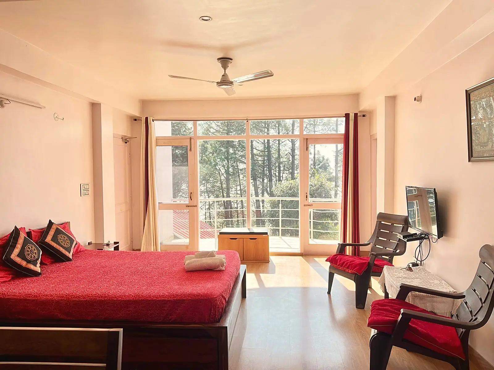 The room, with a red bed, glass doors to the balcony and a wall-mounted TV