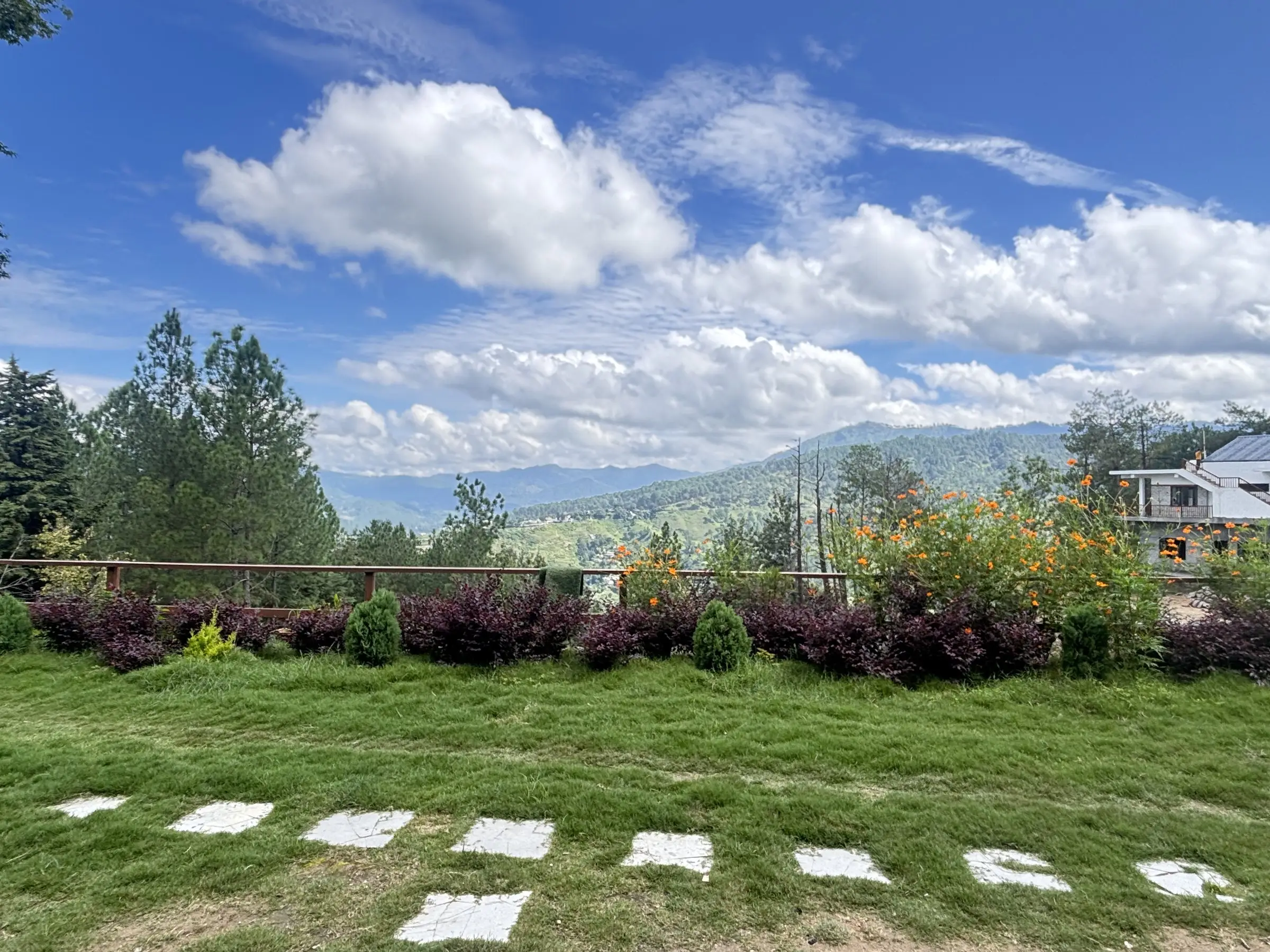 A lawn with stepping stones and shrubs, and hills under big clouds