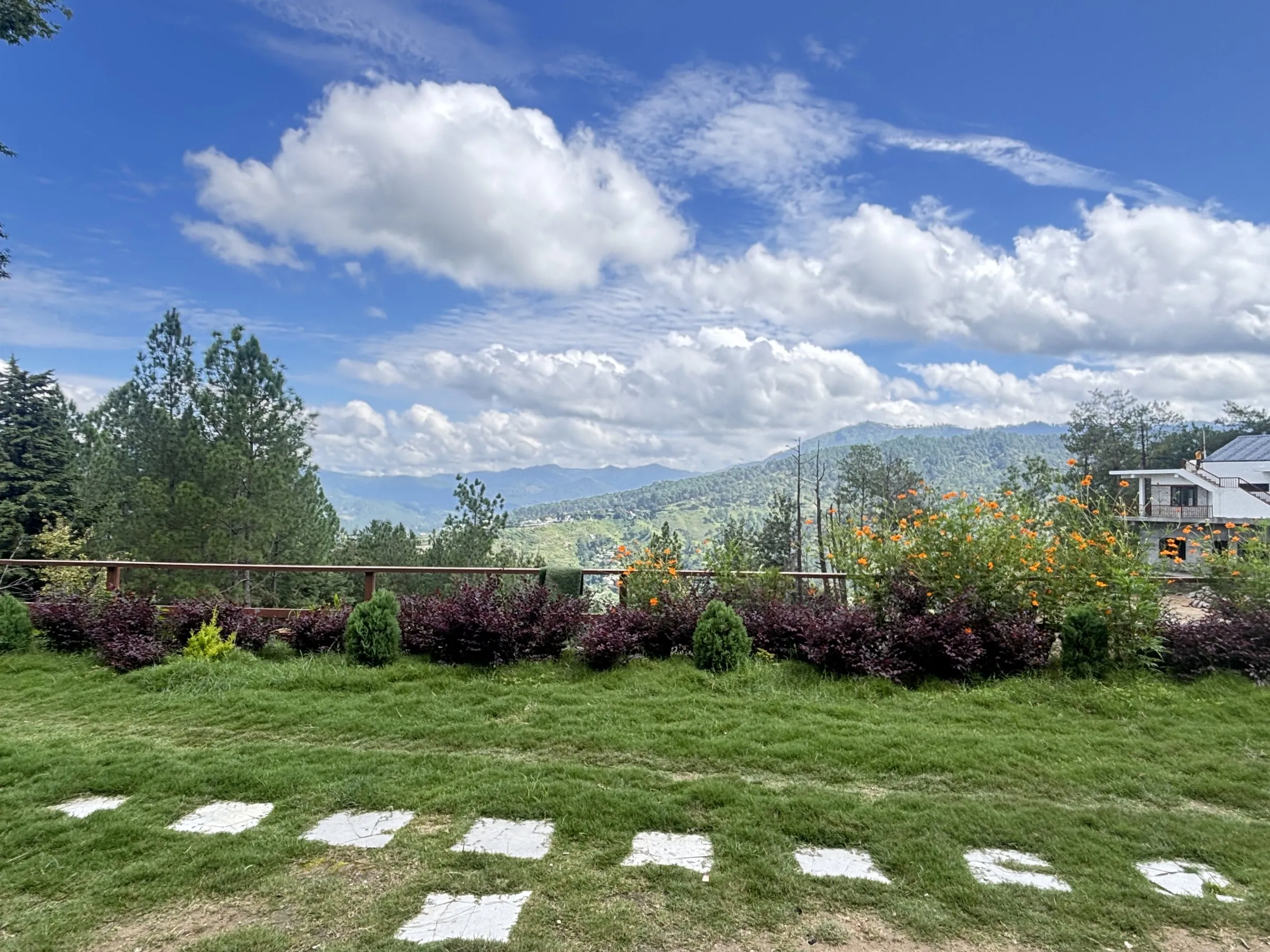 A lawn with stepping stones and shrubs, and hills under big clouds
