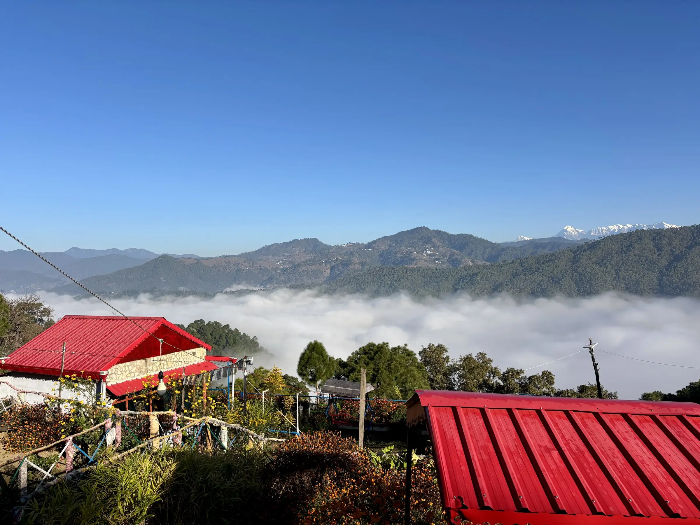 Red tin roofs above a valley filled with cloud, snow peaks beyond