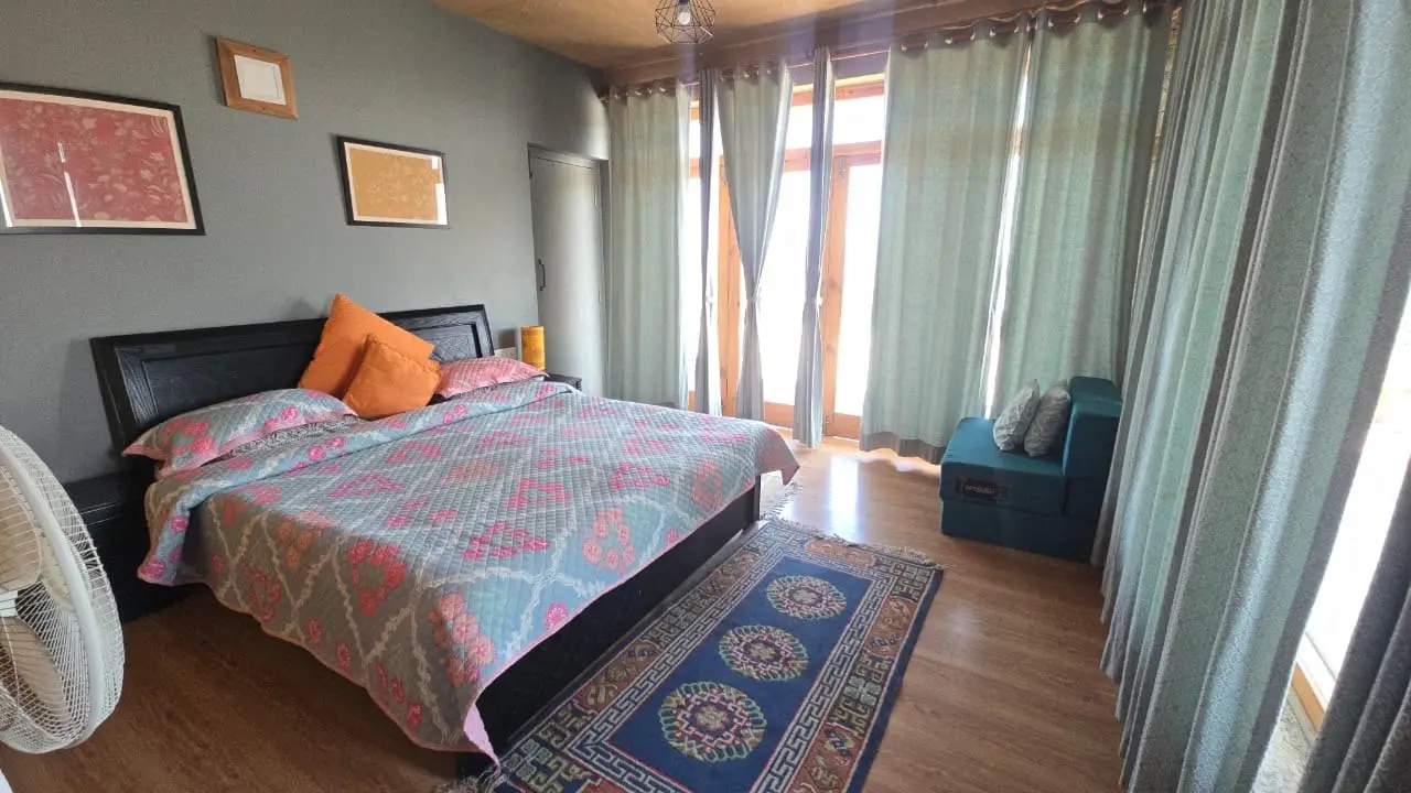 A bedroom with a black bed, a patterned rug and pale curtains