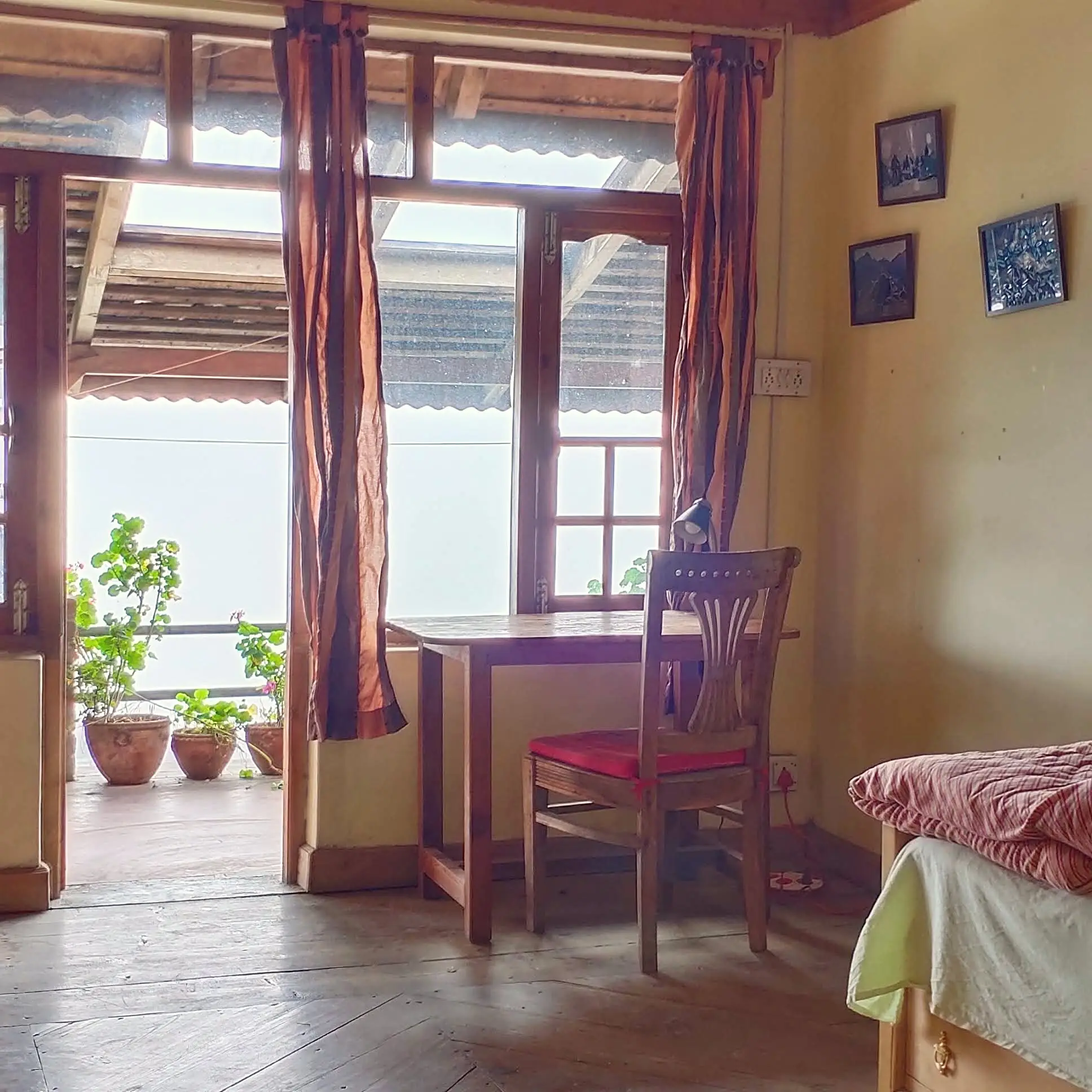 A wooden table and chair by an open balcony door with potted plants