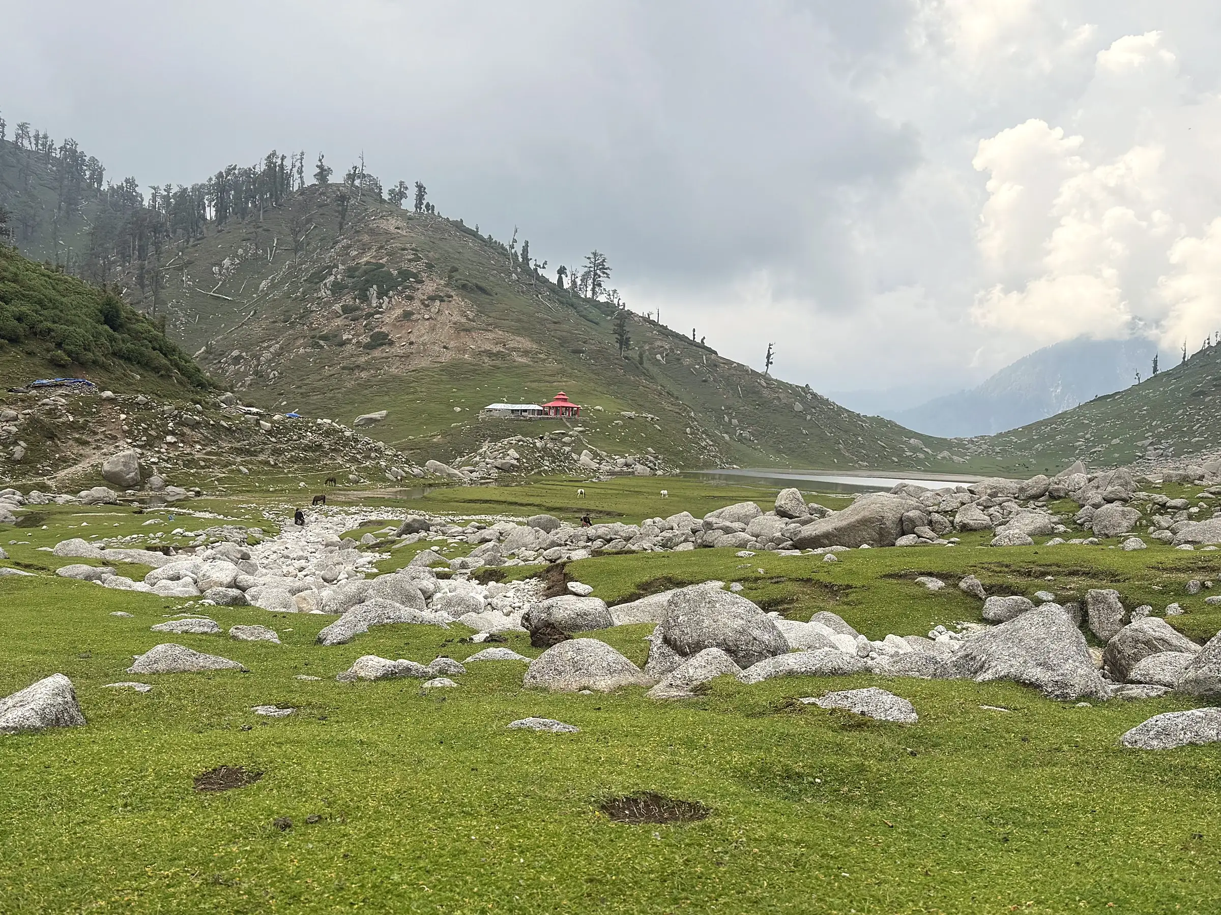 An open meadow of boulders, with a small red-roofed building and a lake beyond