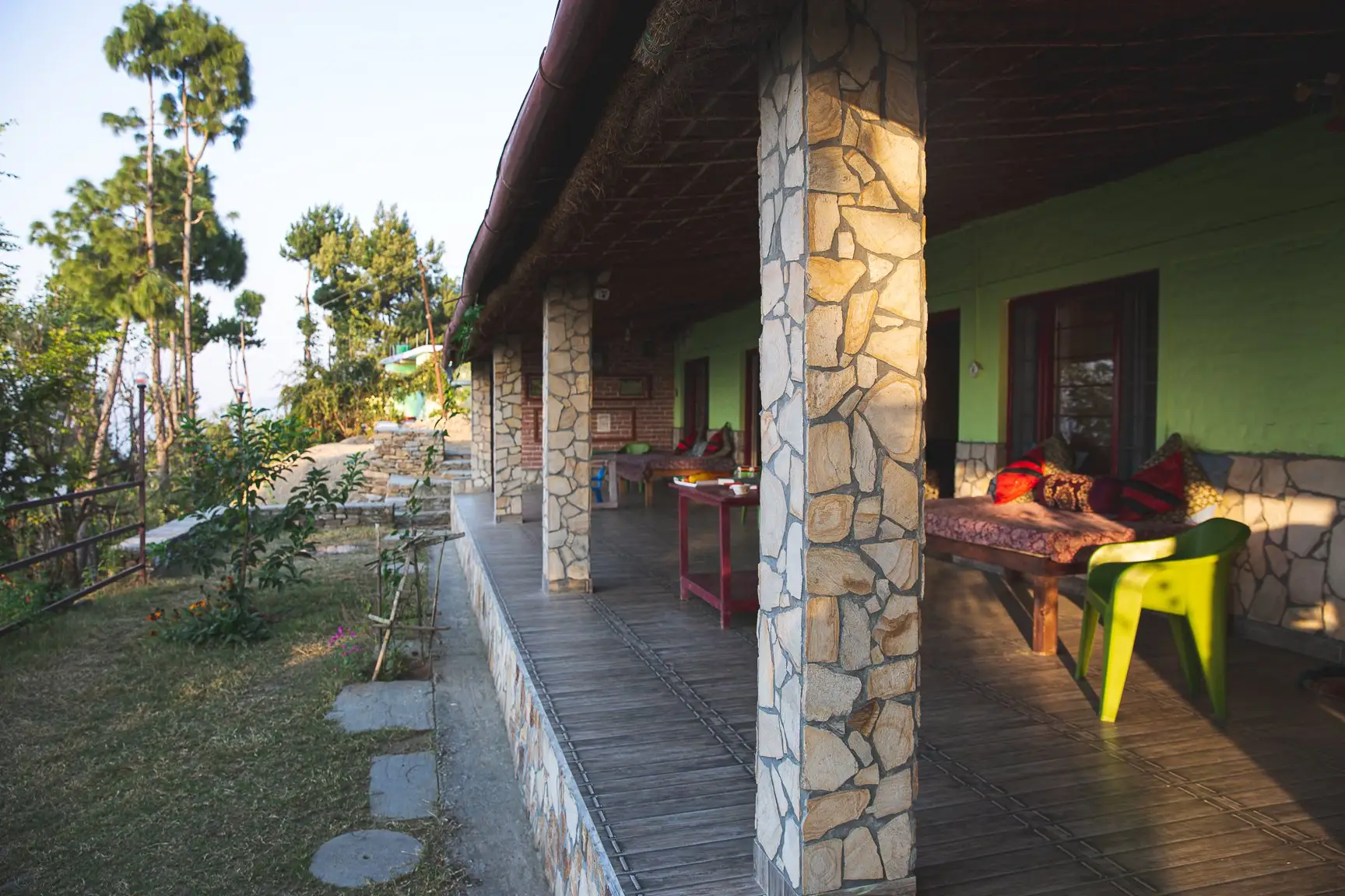 A covered veranda with stone pillars, a wooden deck and a daybed