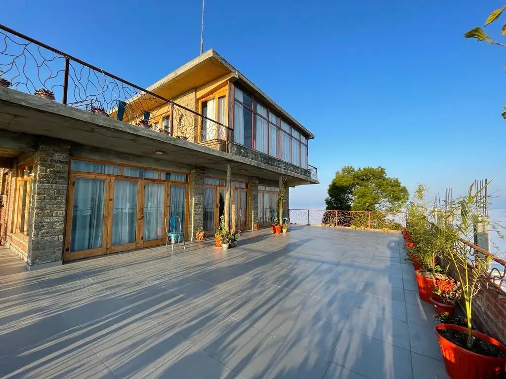 A wide paved terrace beside a stone and timber house, with planters