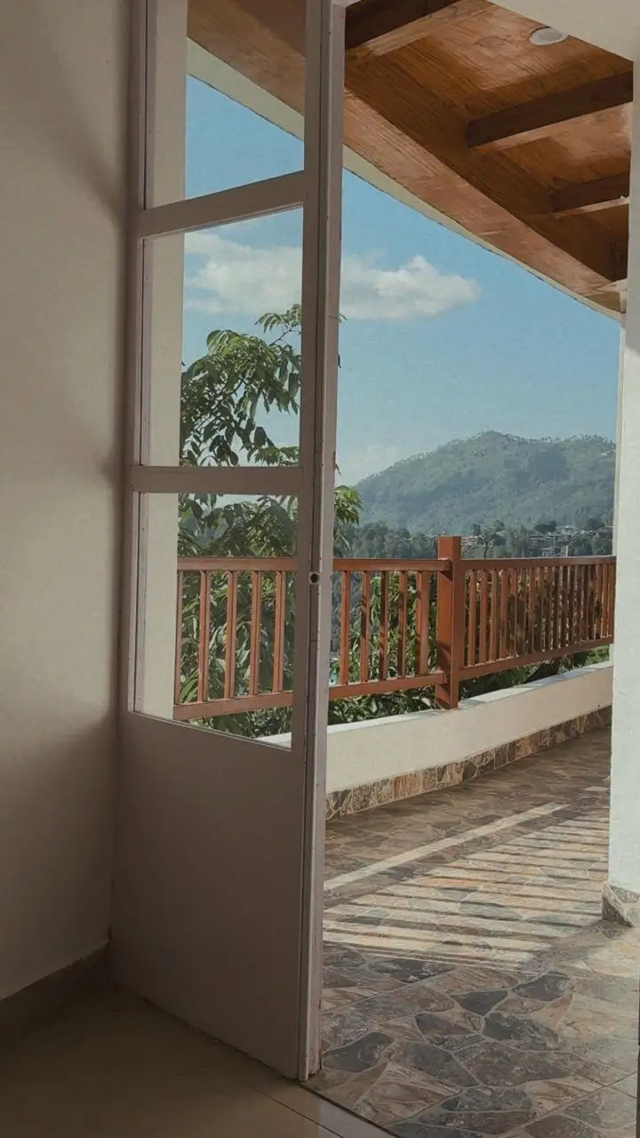 An open glazed door onto a stone balcony facing a green hill