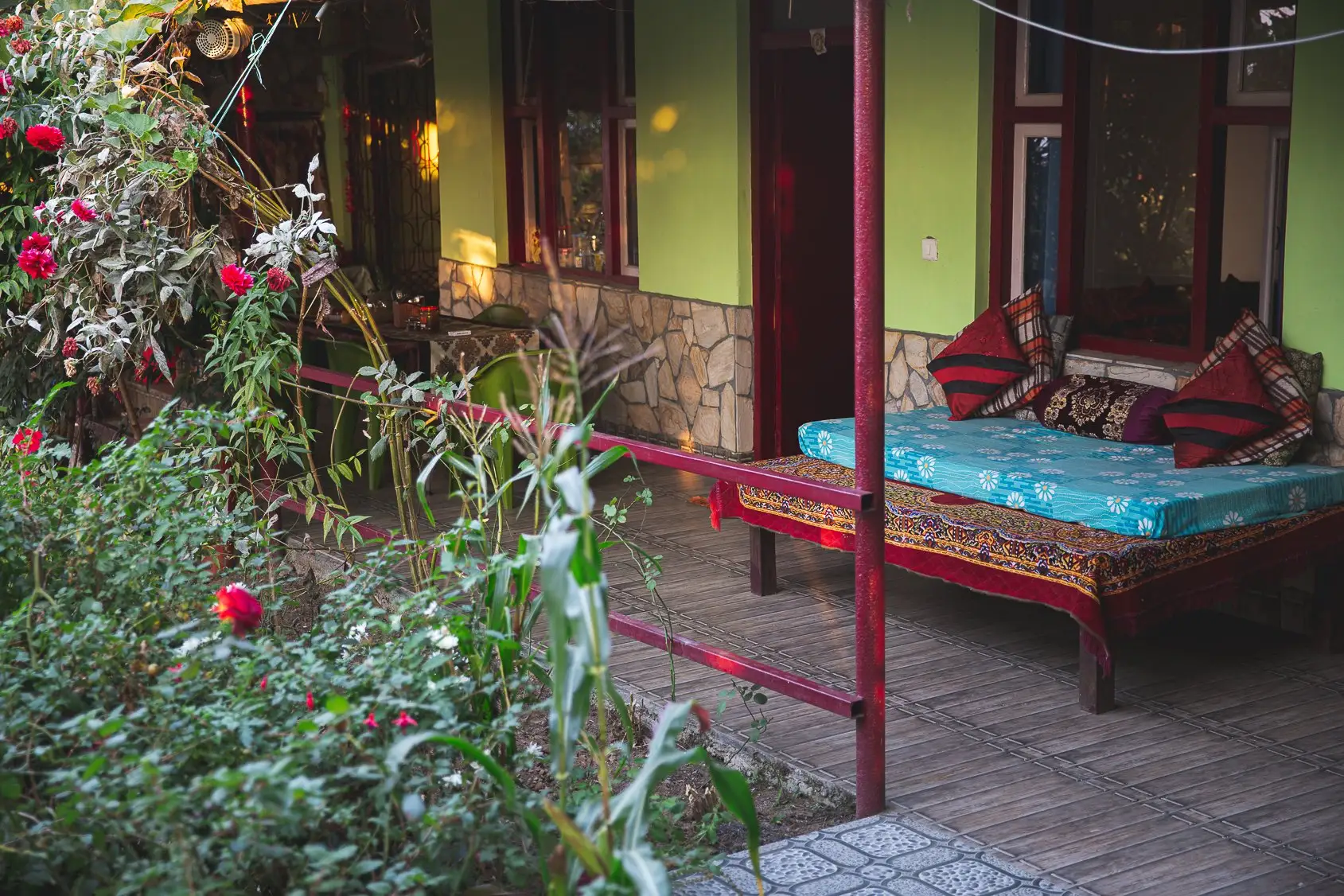 A daybed with red cushions on the veranda, behind rose bushes
