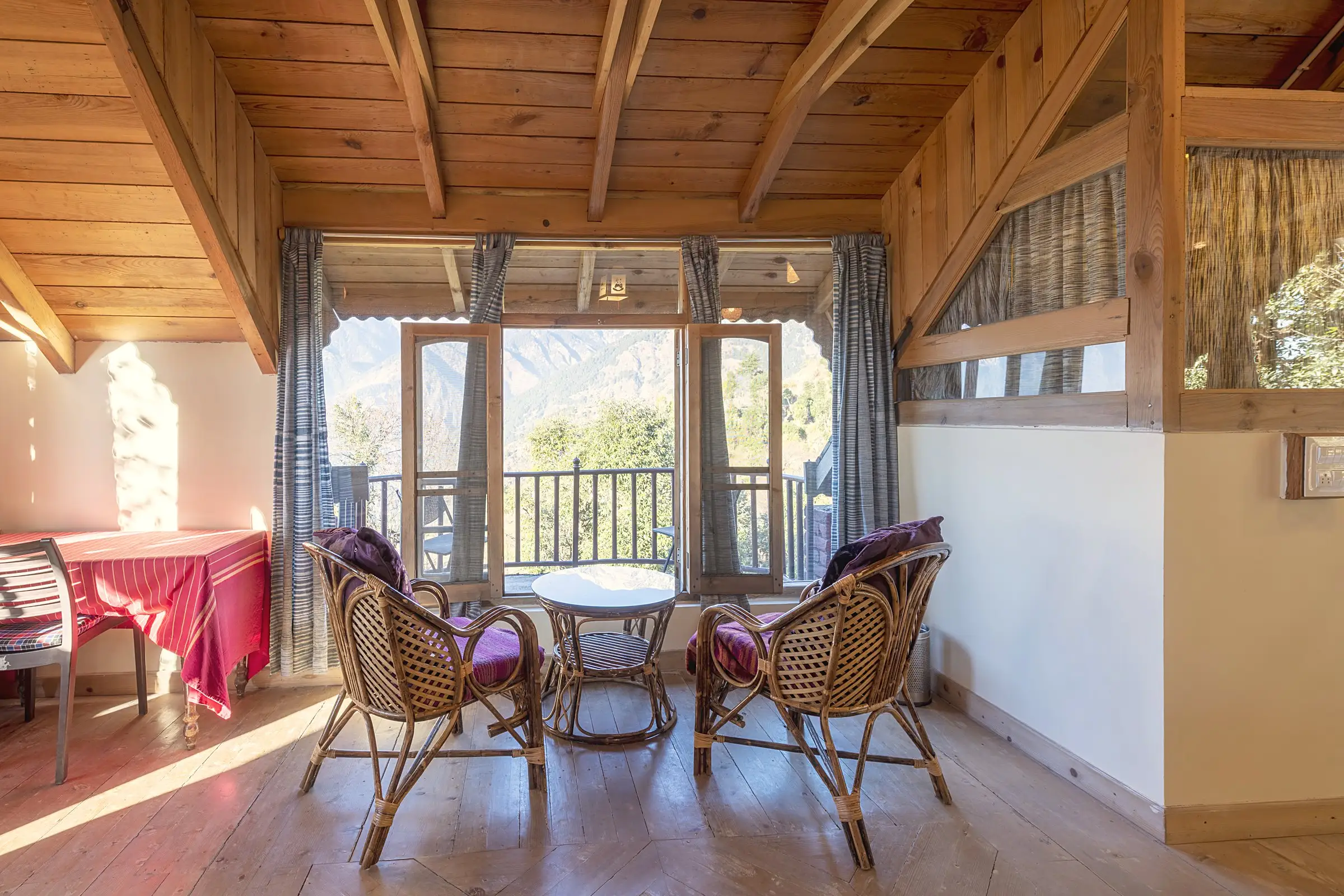 A sitting area with two cane chairs, a round table and a beamed ceiling