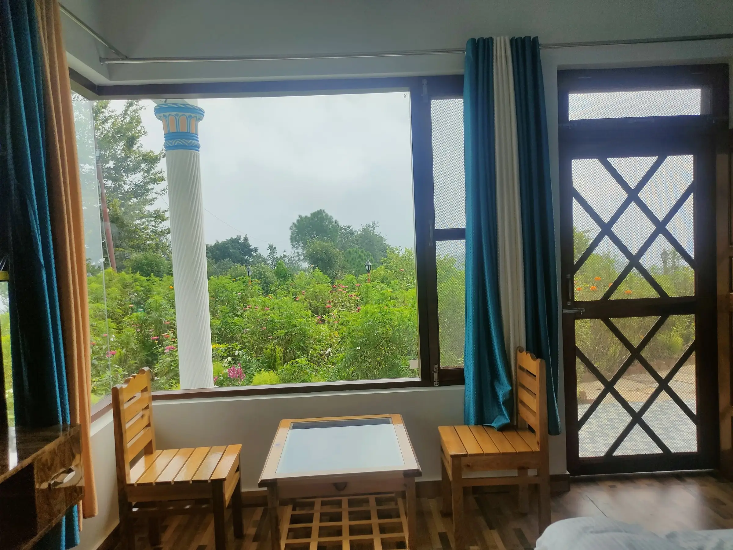 A small table and two wooden chairs at a window onto the garden