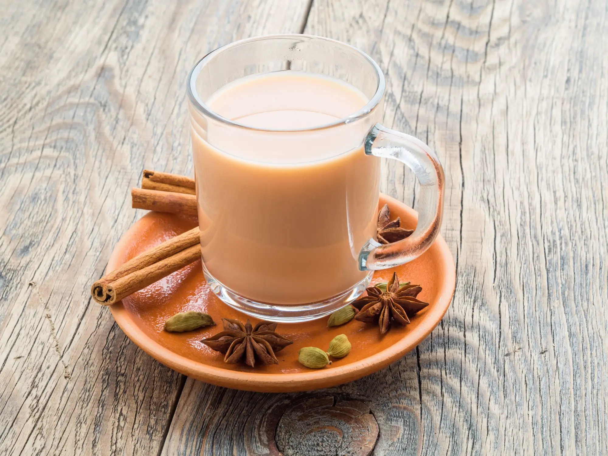 A clear mug of spiced chai on a wooden table