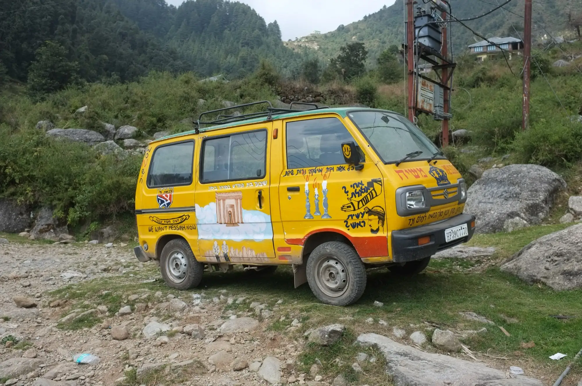 A yellow van parked on a stony track where the road ends in Dharamkot