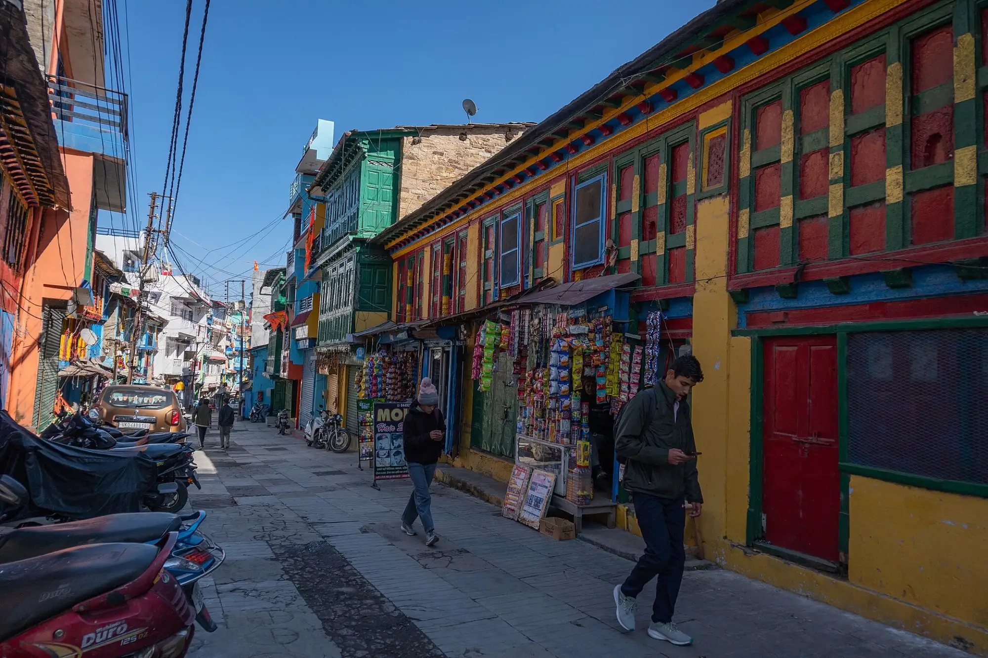 A lane of painted wooden shopfronts in Almora bazaar with shoppers walking