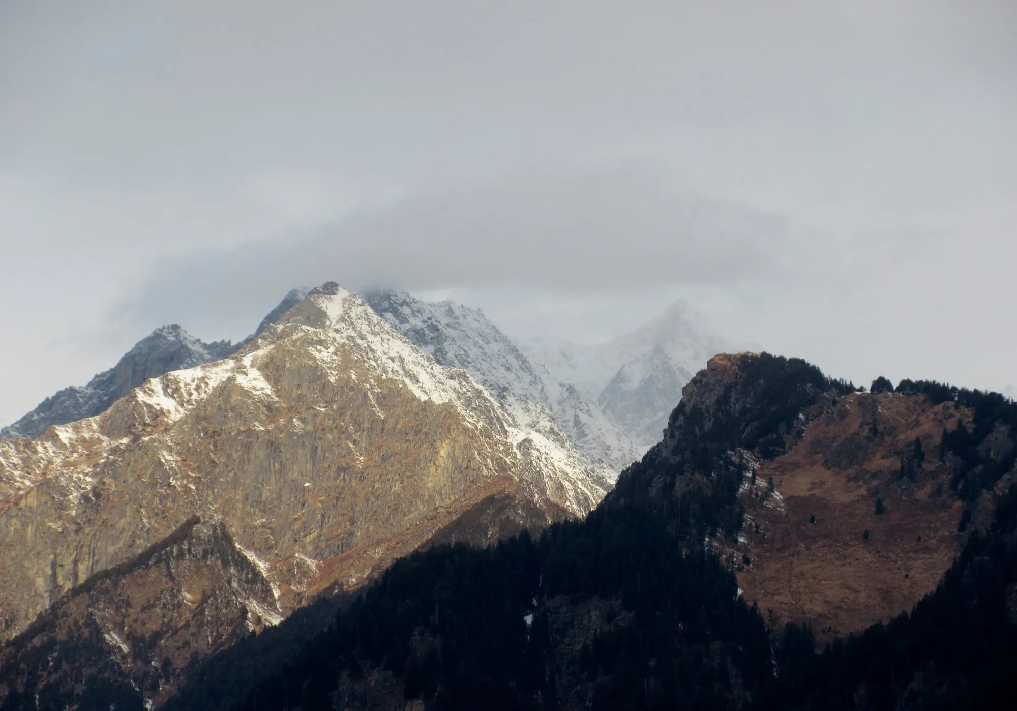 Snow on a mountain ridge above dark slopes under a grey sky