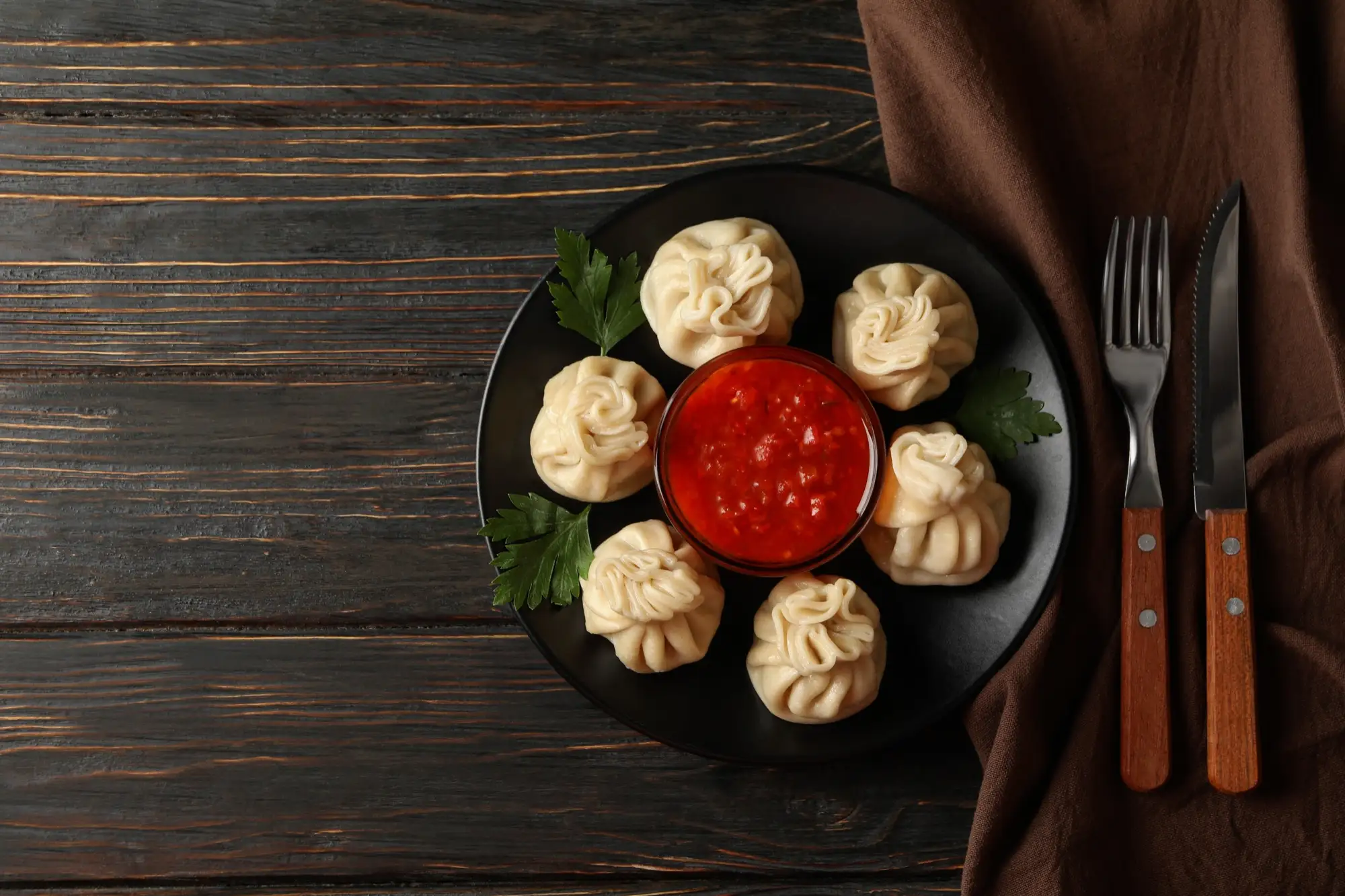 Steamed momos with red sauce on a dark plate, on a wooden table