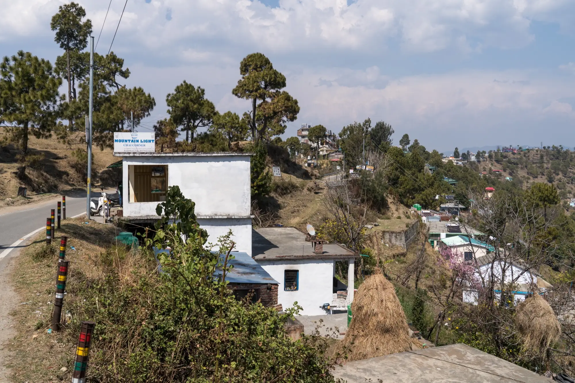 Houses just below a hill road at Kasar Devi, with a tea stall by the roadside