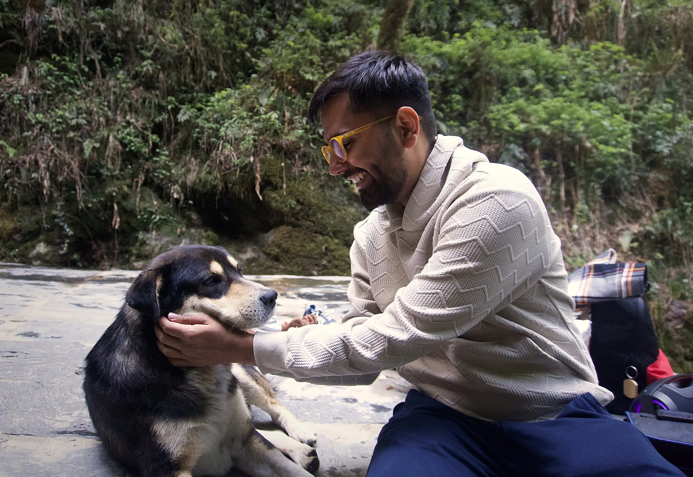 Sarthak sitting on a stone path in the hills, petting a dog