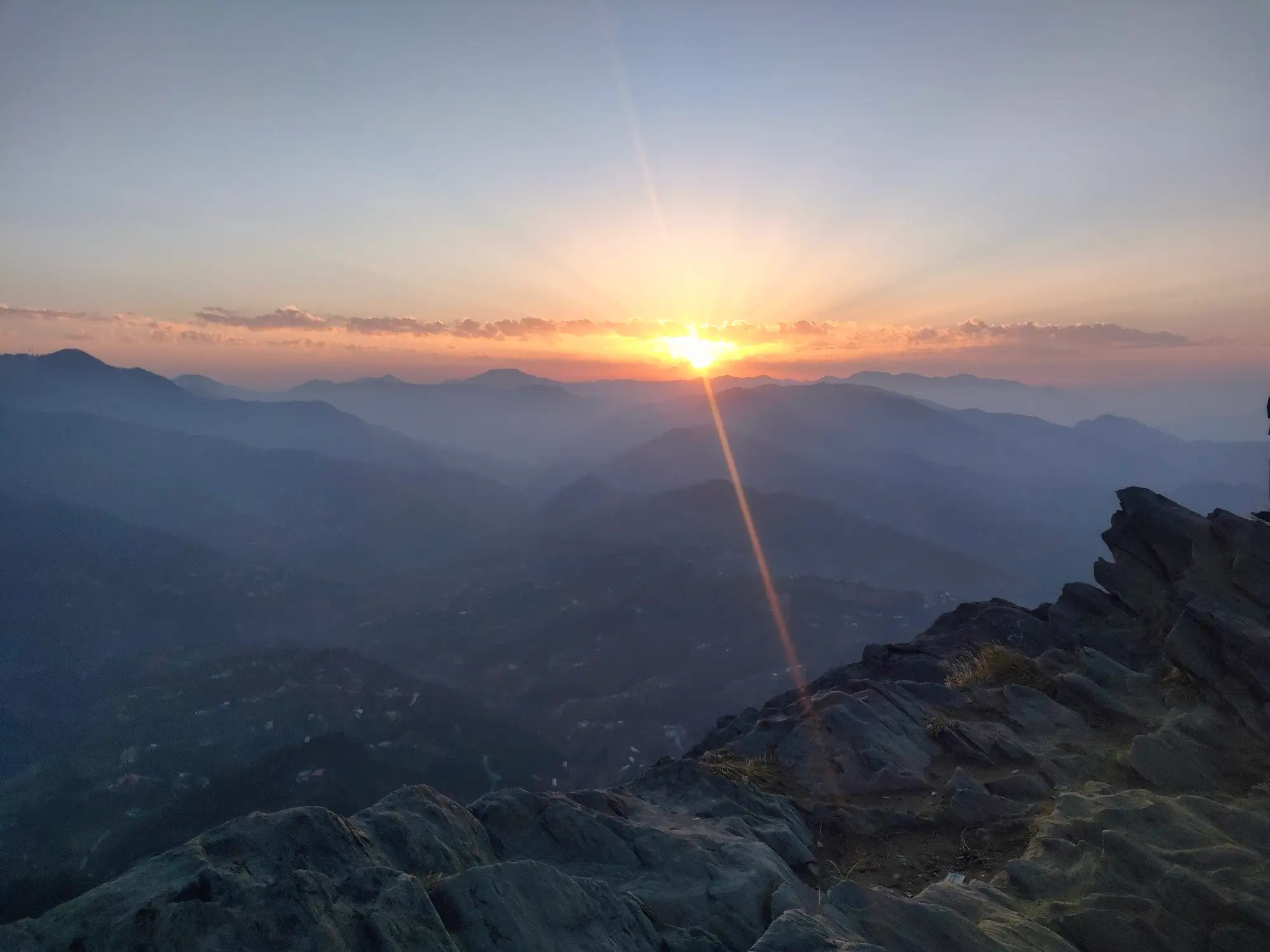 The sun setting over layered hills from a rocky point at Mukteshwar